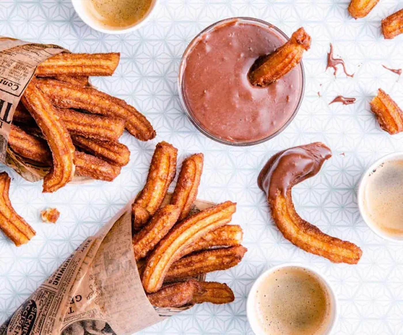 Churros dorés dans leur cornet, avec une coupe de chocolat fondu.