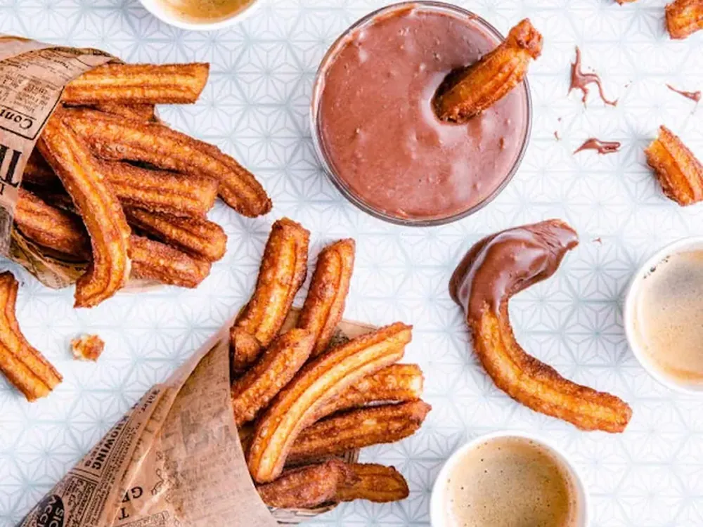 Churros dorés dans leur cornet, avec une coupe de chocolat fondu.